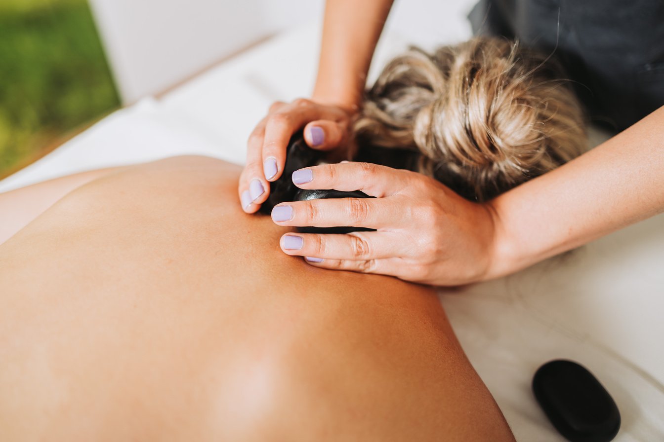 Therapist placing hot spa volcanic lava stone on a female patient's neck. Energy stones.